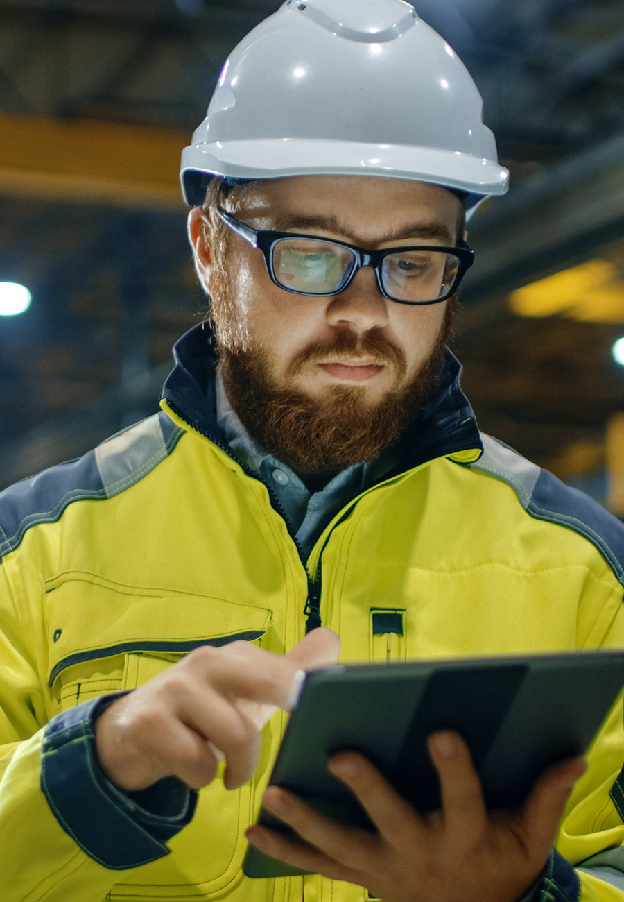 Man in a factory wearing a hard hat and working on a tablet