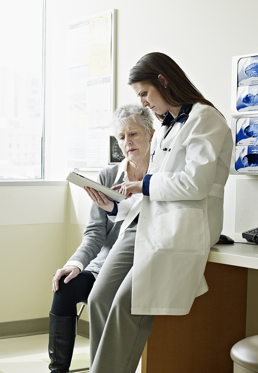 A female doctor in a hospital room reviewing a digital chart with a female patient